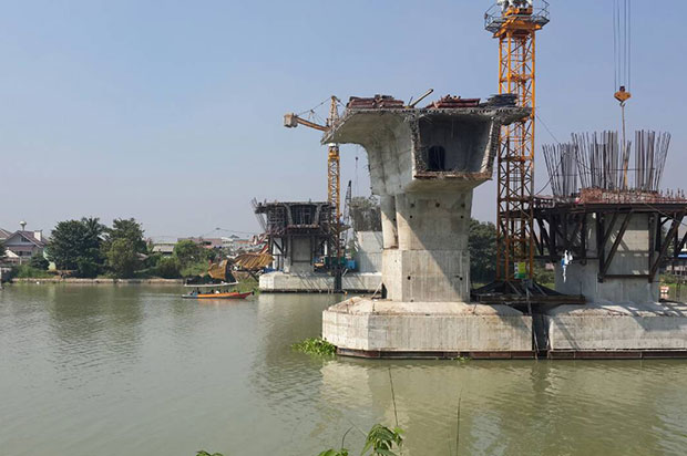 The toppled crane lies to the left of the far bridge pillar at the construction site on the Chao Phraya river bank between tambon Ko Rian and tambon Samphao Lom in Ayutthaya on Tuesday