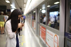 A woman checks her mobile phone while waiting for the train arrival at an underground station in Bangkok.